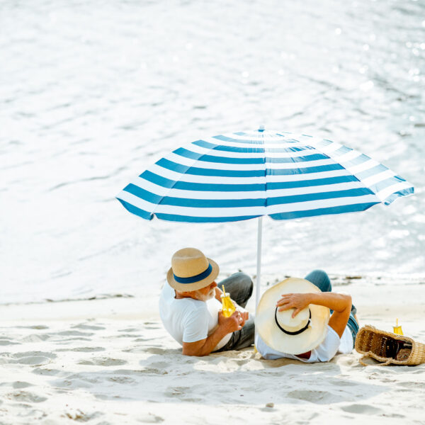 Two seniors laying on beach under umbrella